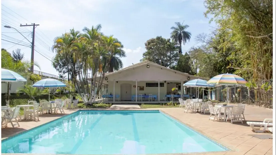 Piscina com palmeiras e a sede ao fundo, em unidade de reabilitação da região de Pará de Minas - MG